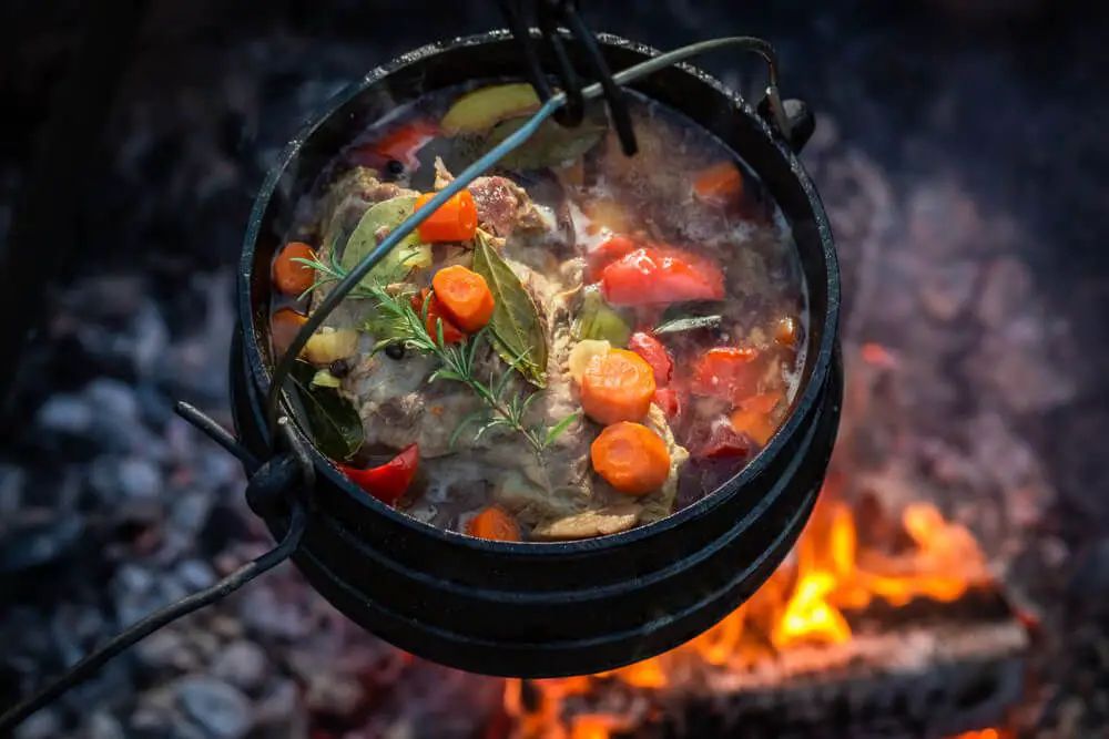 Cooking on a cast iron pot hanging on a tripod placed over a camp fire